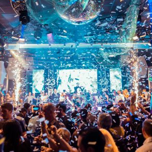 Vibrant nightclub scene in Mantua, Italy, featuring a lively crowd, confetti, and colorful lights.